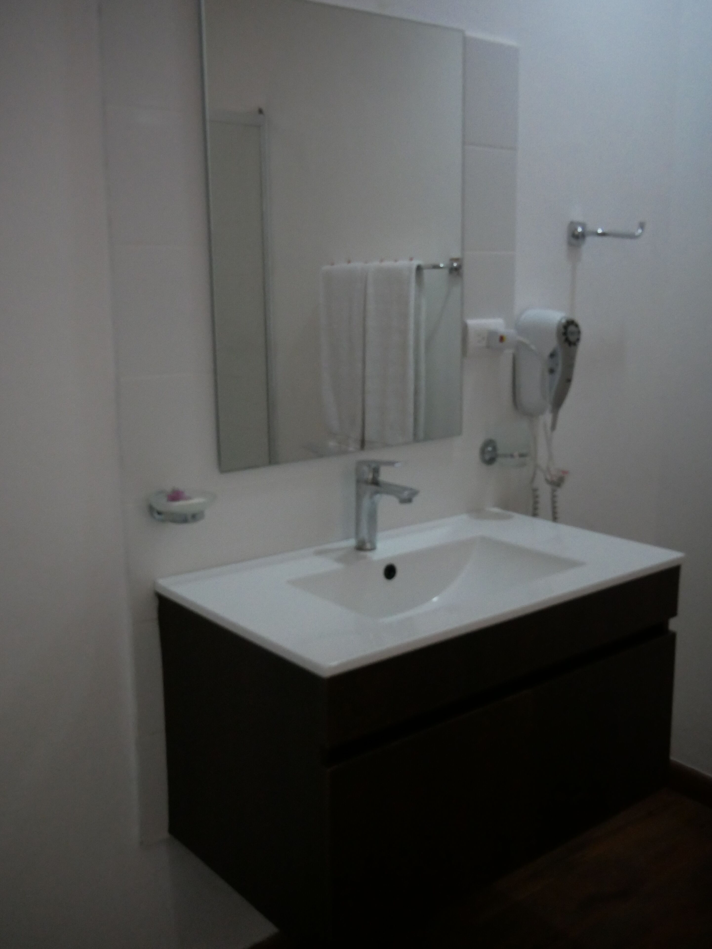 Un baño con lavamanos blanco, espejo, toallero y secador de pelo.
