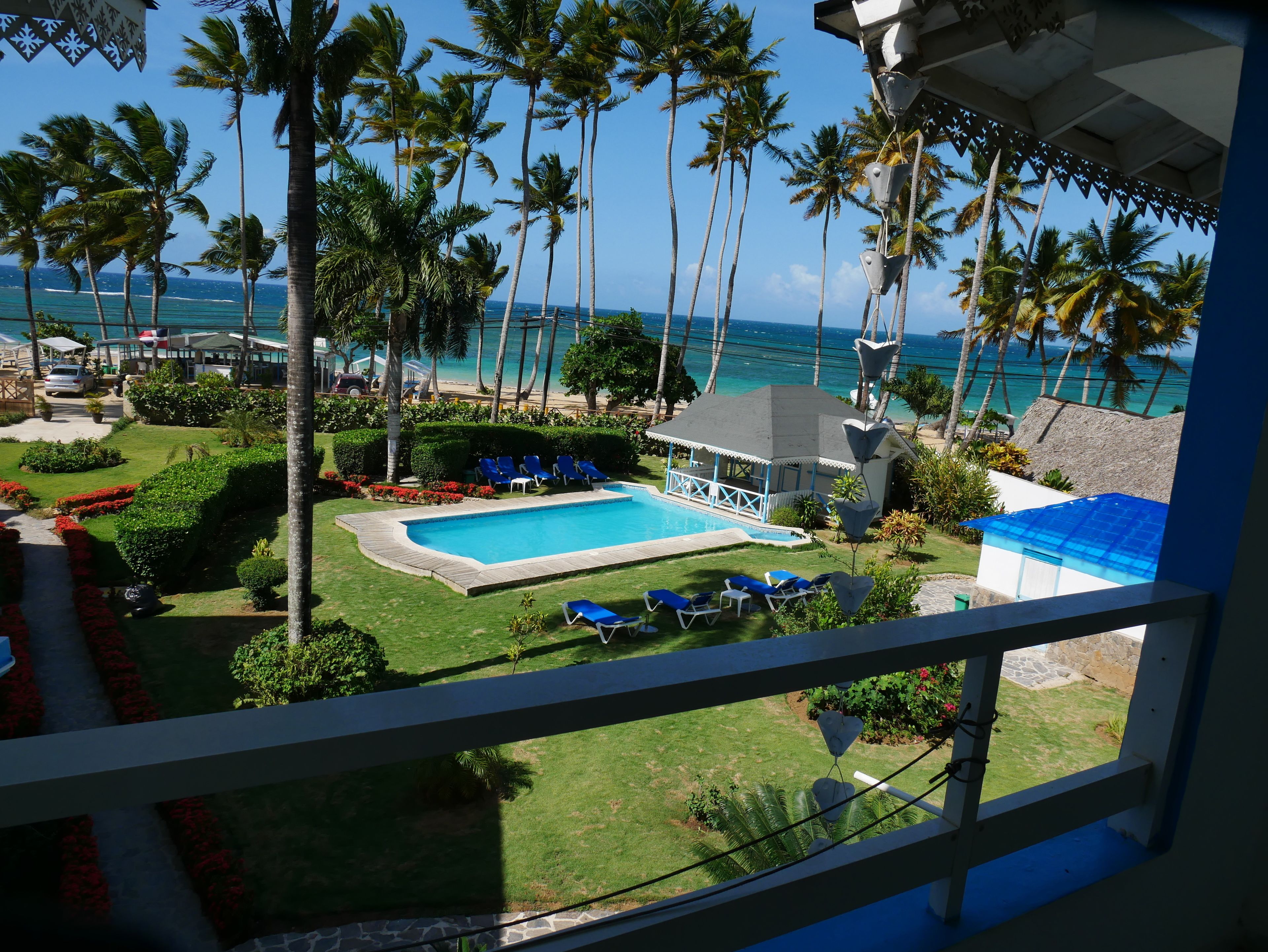 Uma área de piscina com vista para o oceano, cercada por palmeiras e um pequeno edifício.