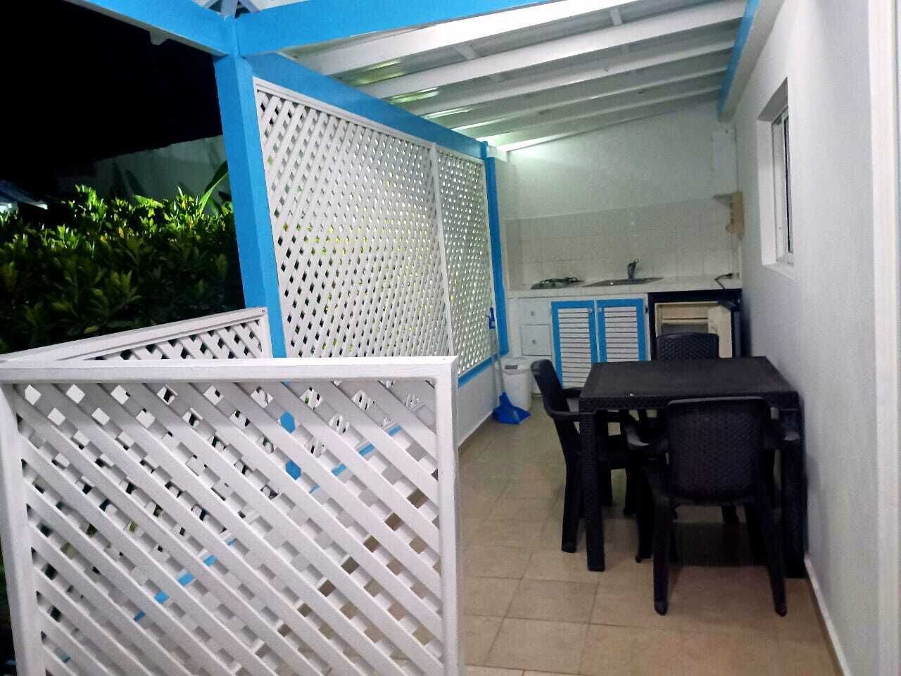 An outdoor patio area with a table and chairs, a white partition, and a blue ceiling.