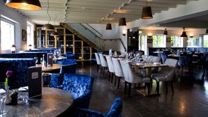 Un restaurante con asientos de terciopelo azul, mesas de madera e iluminación colgante.