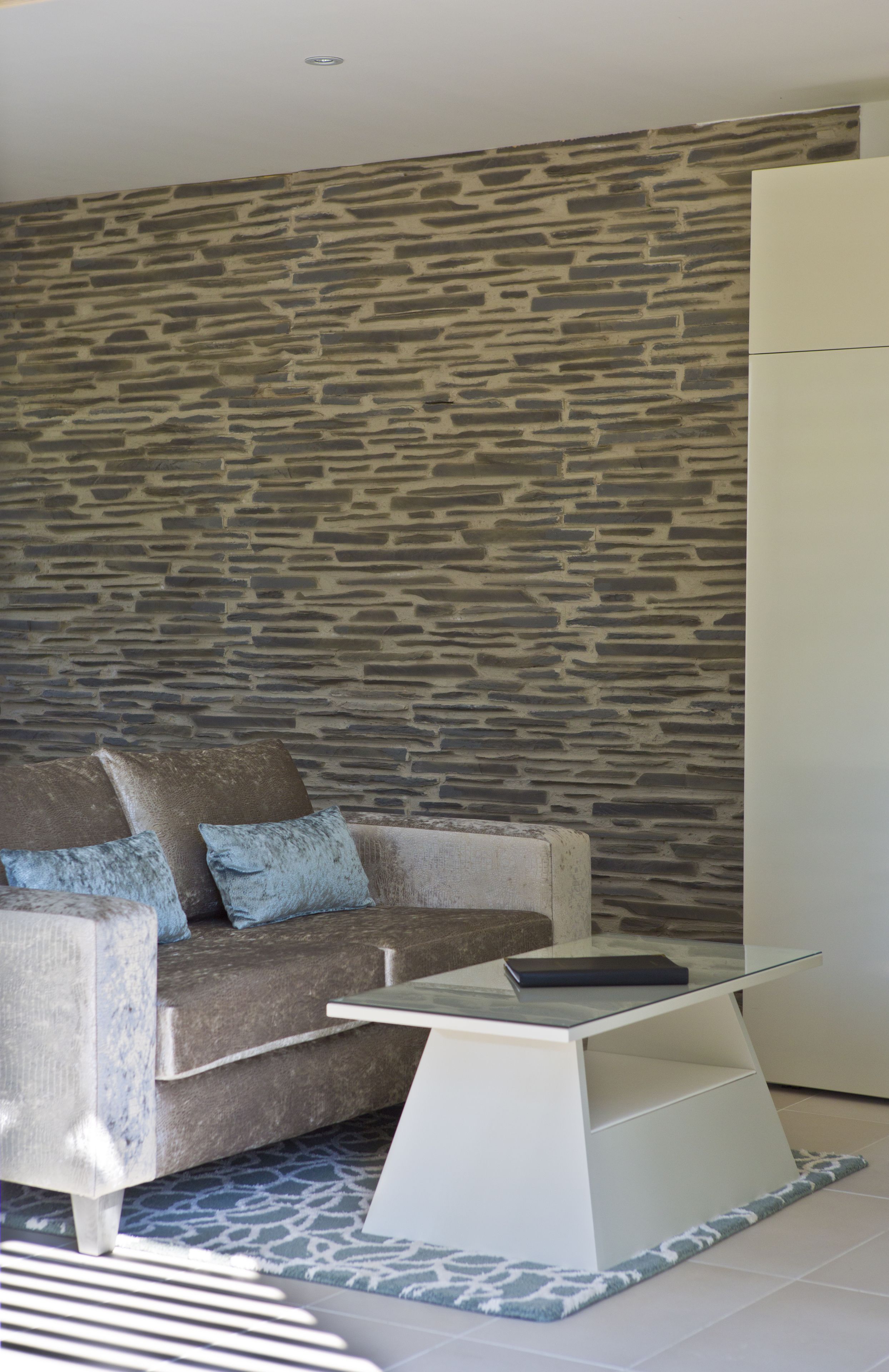 A modern living room with a stone-patterned wall, a sofa with cushions, and a glass-top coffee table.