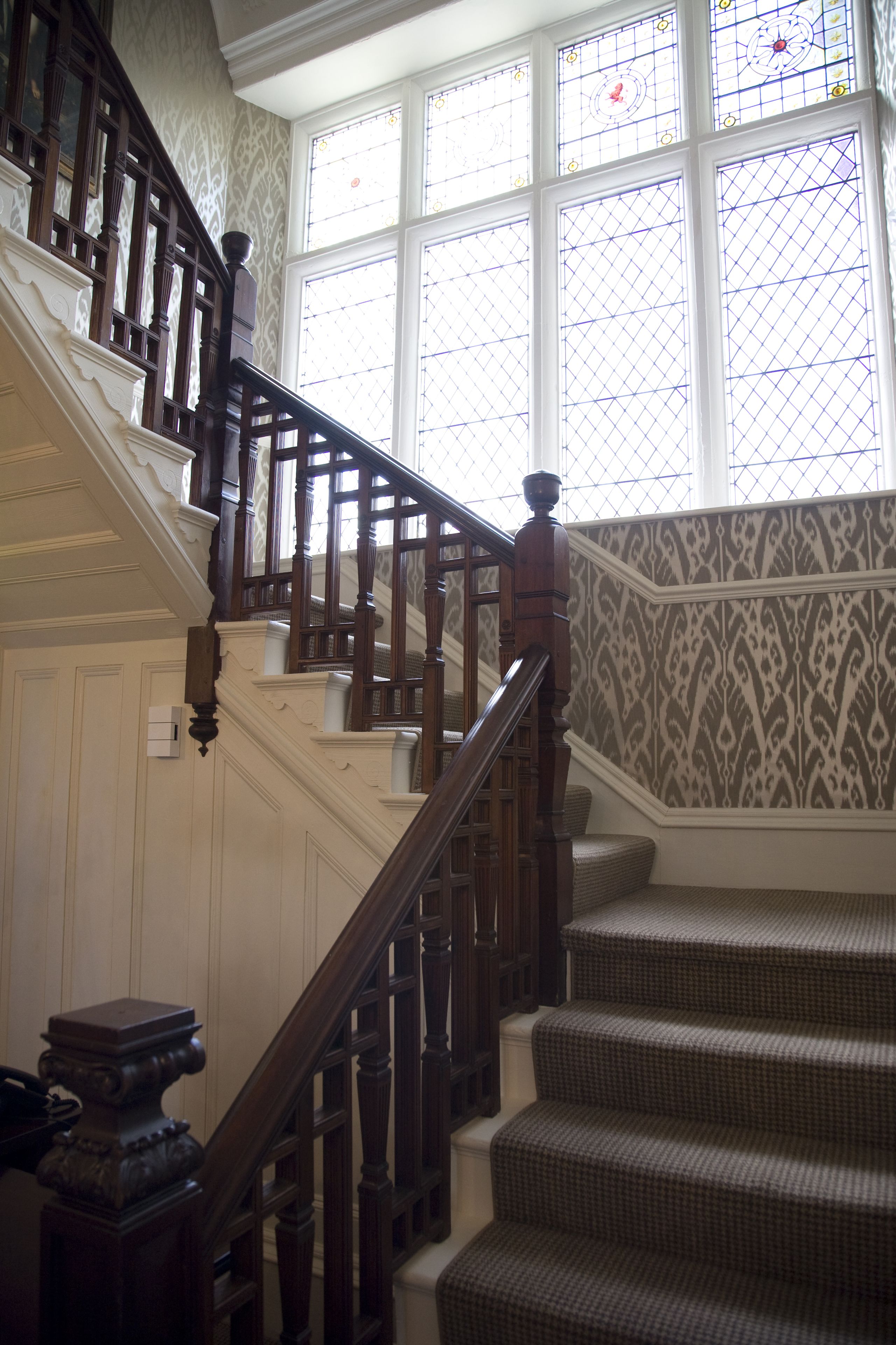 A grand staircase with wooden railings and patterned wallpaper.