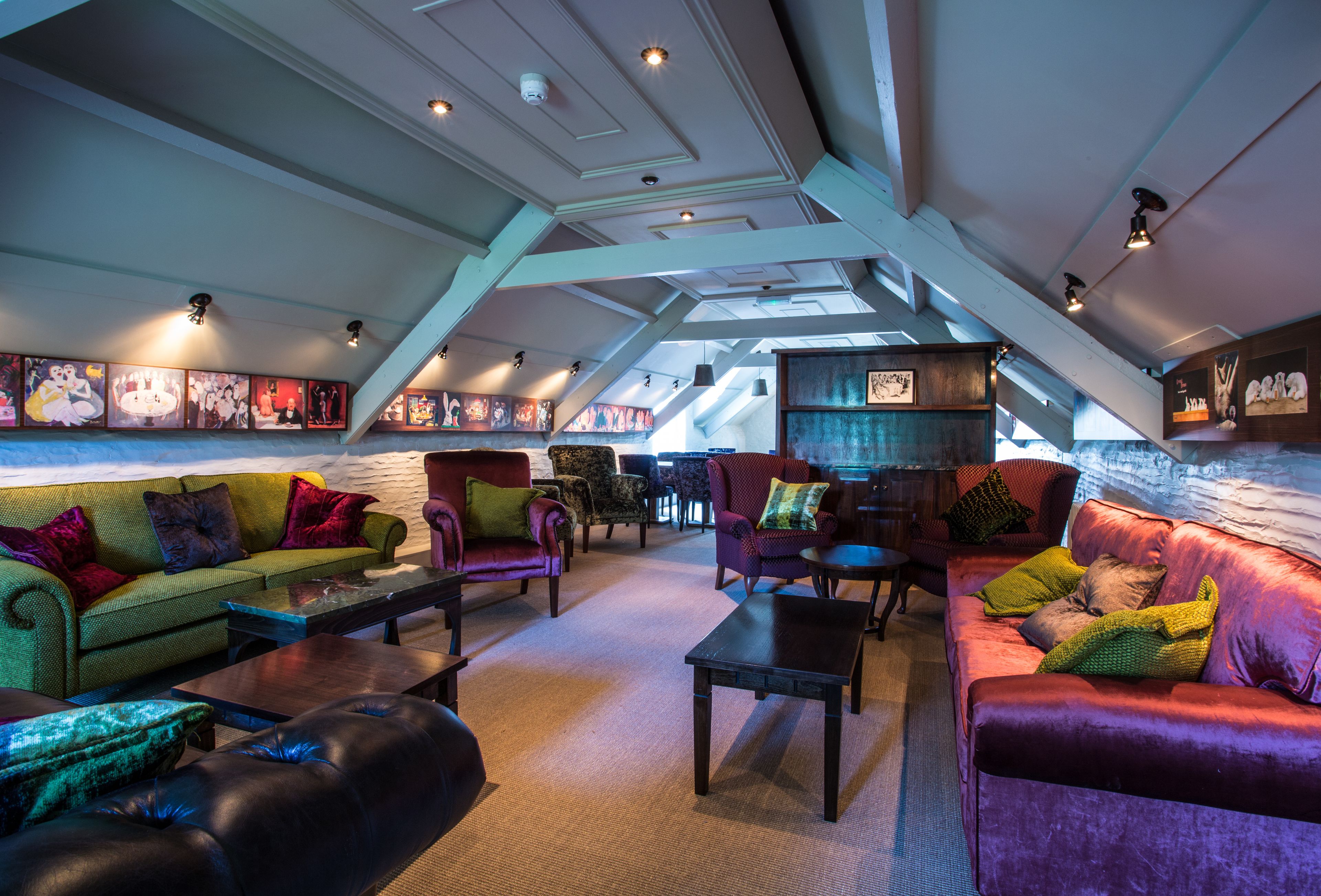 A spacious loft-style room with a sloped ceiling, featuring a green sofa, a red sofa, and multiple armchairs.