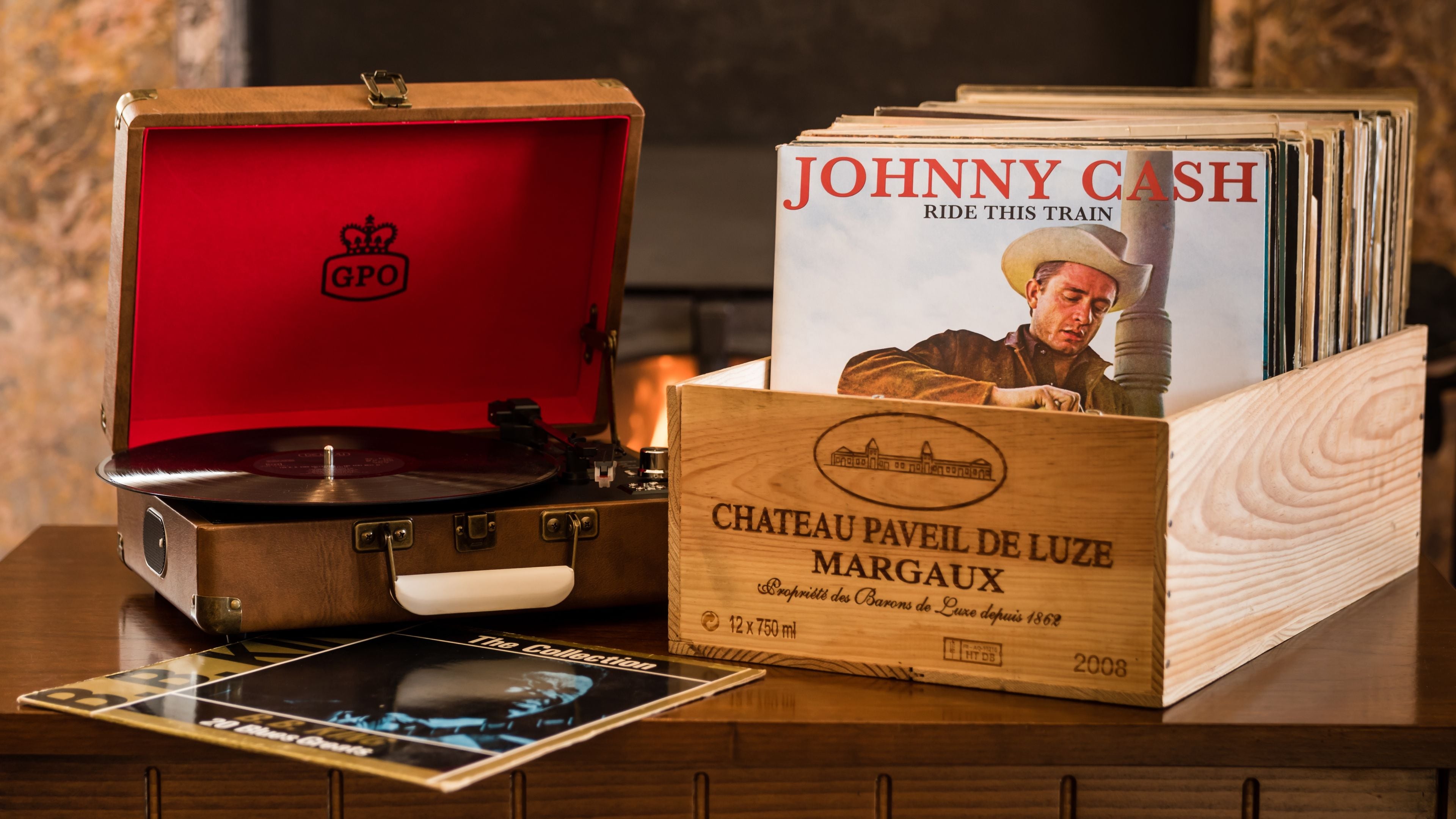 Un vieux tourne-disque, une boîte en bois portant l’inscription « CHATEAU PAVEIL DE LUZE MARGAUX », et une pile de disques vinyle.