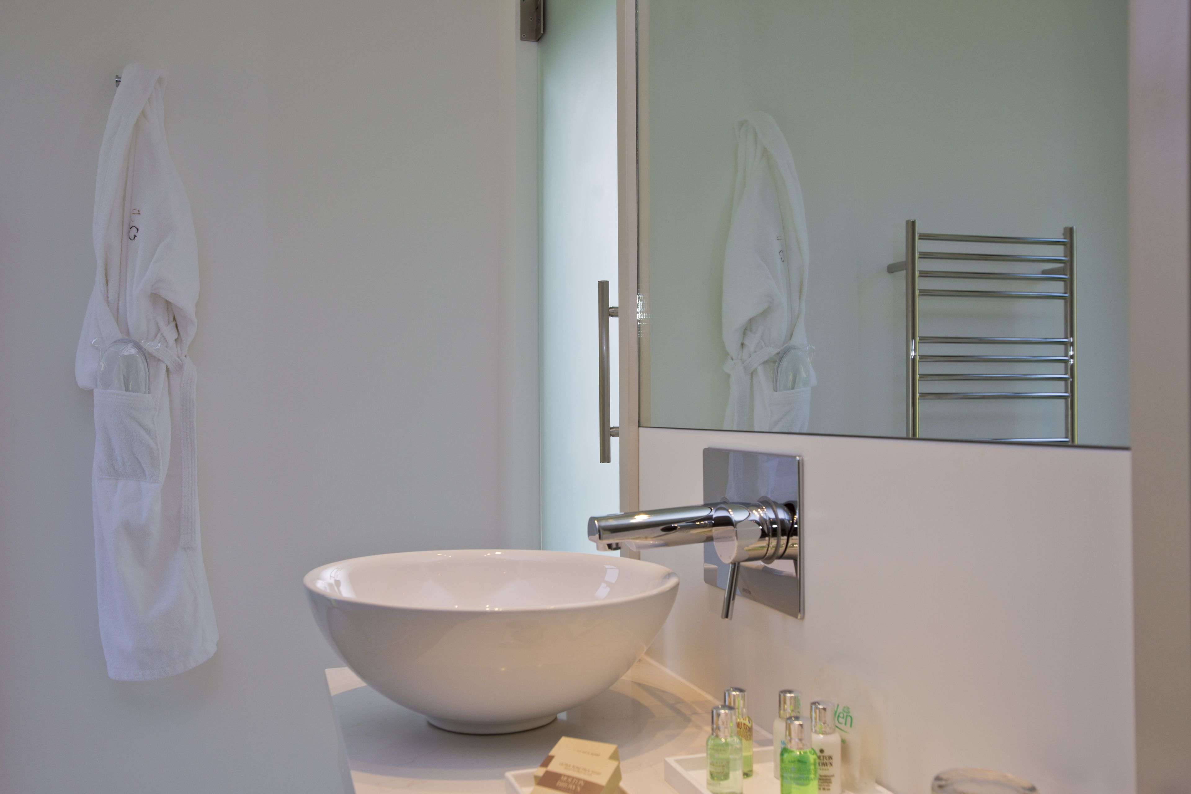 A bathroom with a large white sink, a mirror, and a towel rack.