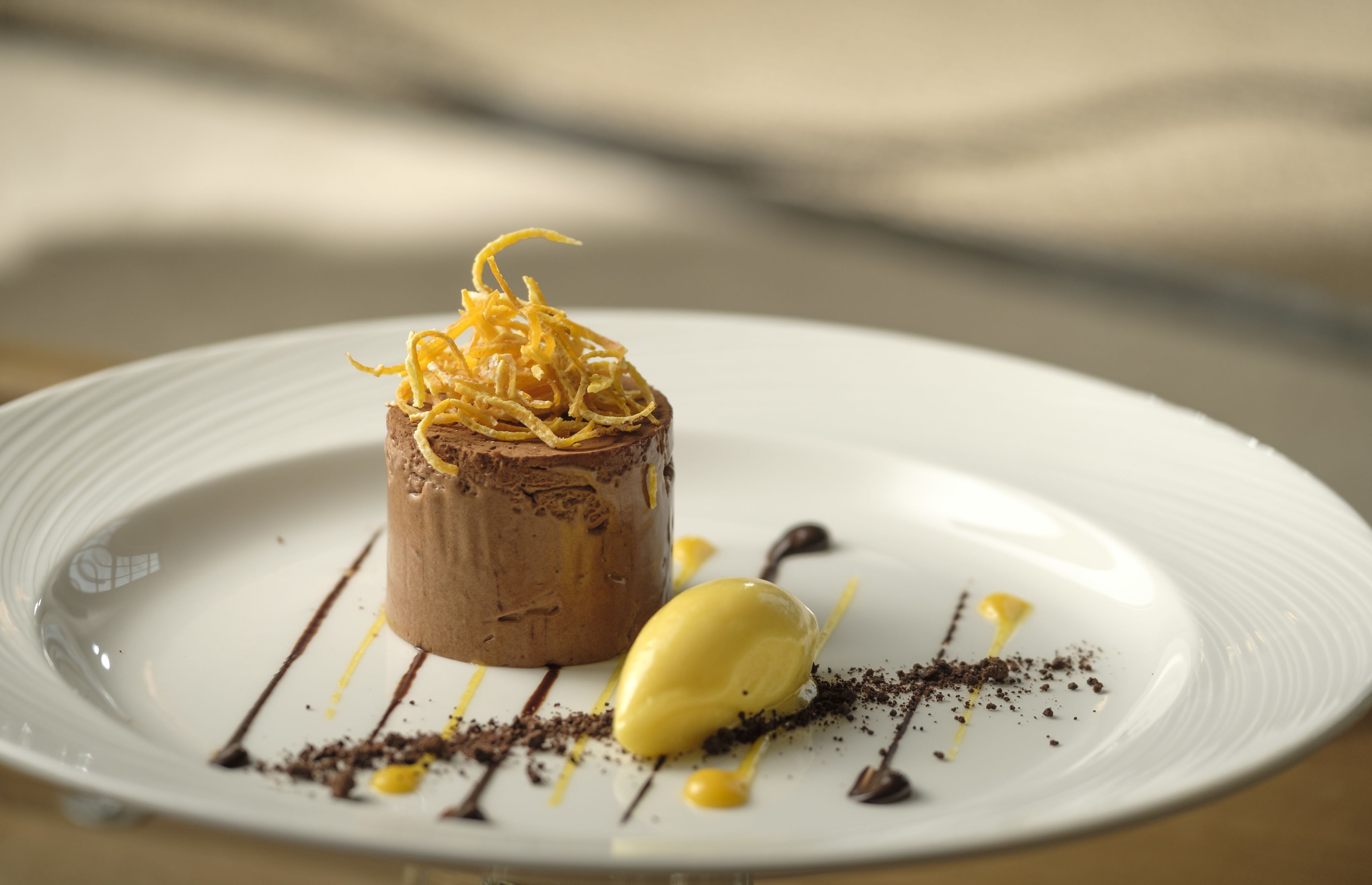A dessert on a white plate with chocolate mousse, a scoop of vanilla ice cream, and chocolate drizzle.