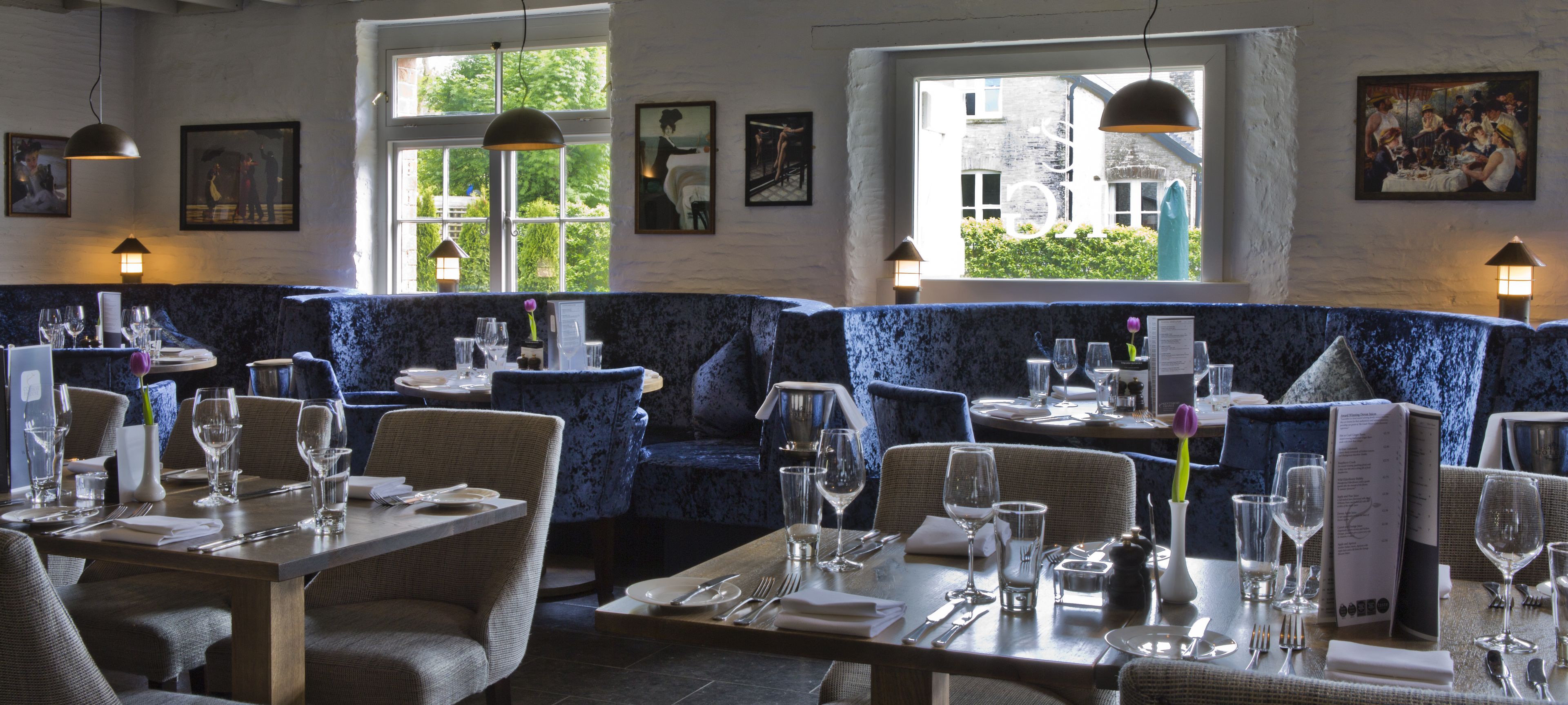 A restaurant with blue upholstered booths, wooden tables, and a view of greenery outside.