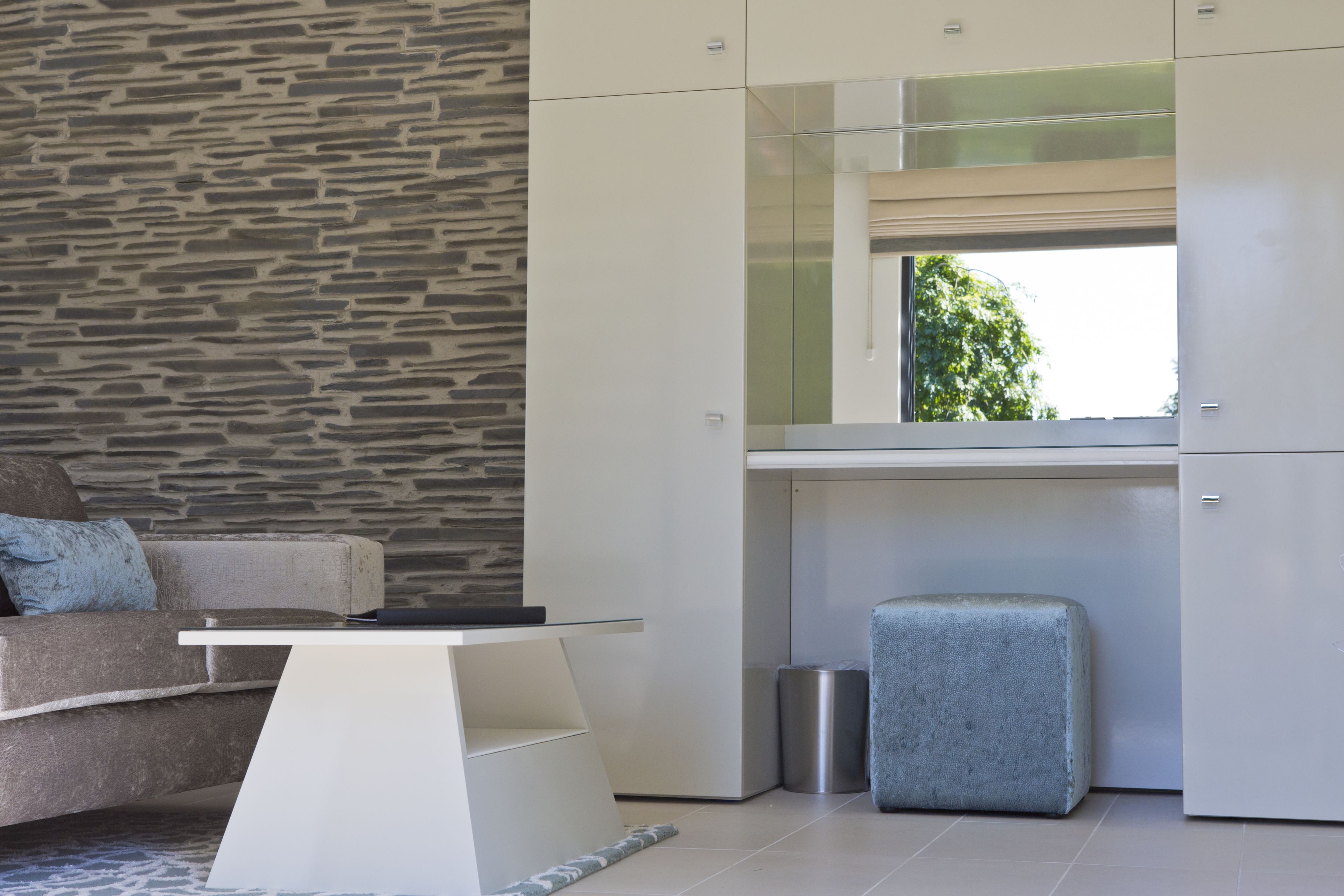 A modern living room with a stone wall, a sofa, a coffee table, and a kitchen area with cabinets and a window.