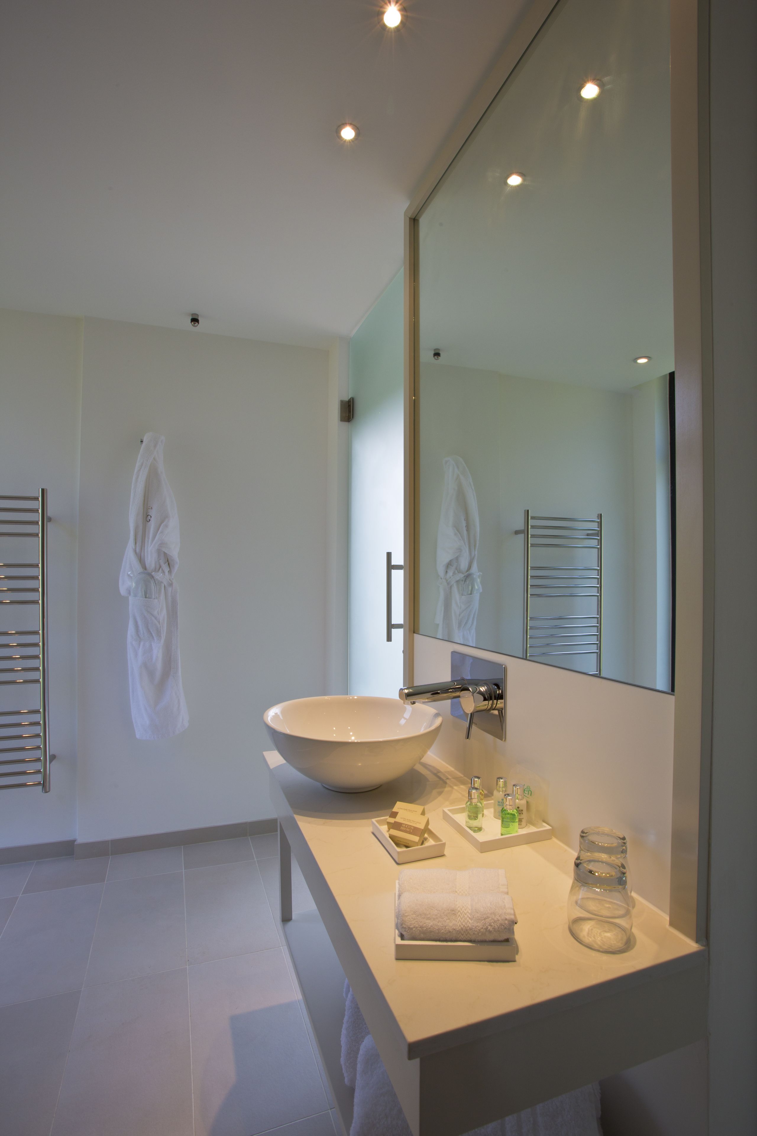 A modern bathroom with a large mirror, a bowl sink, a towel rack, and a glass jar on the countertop.