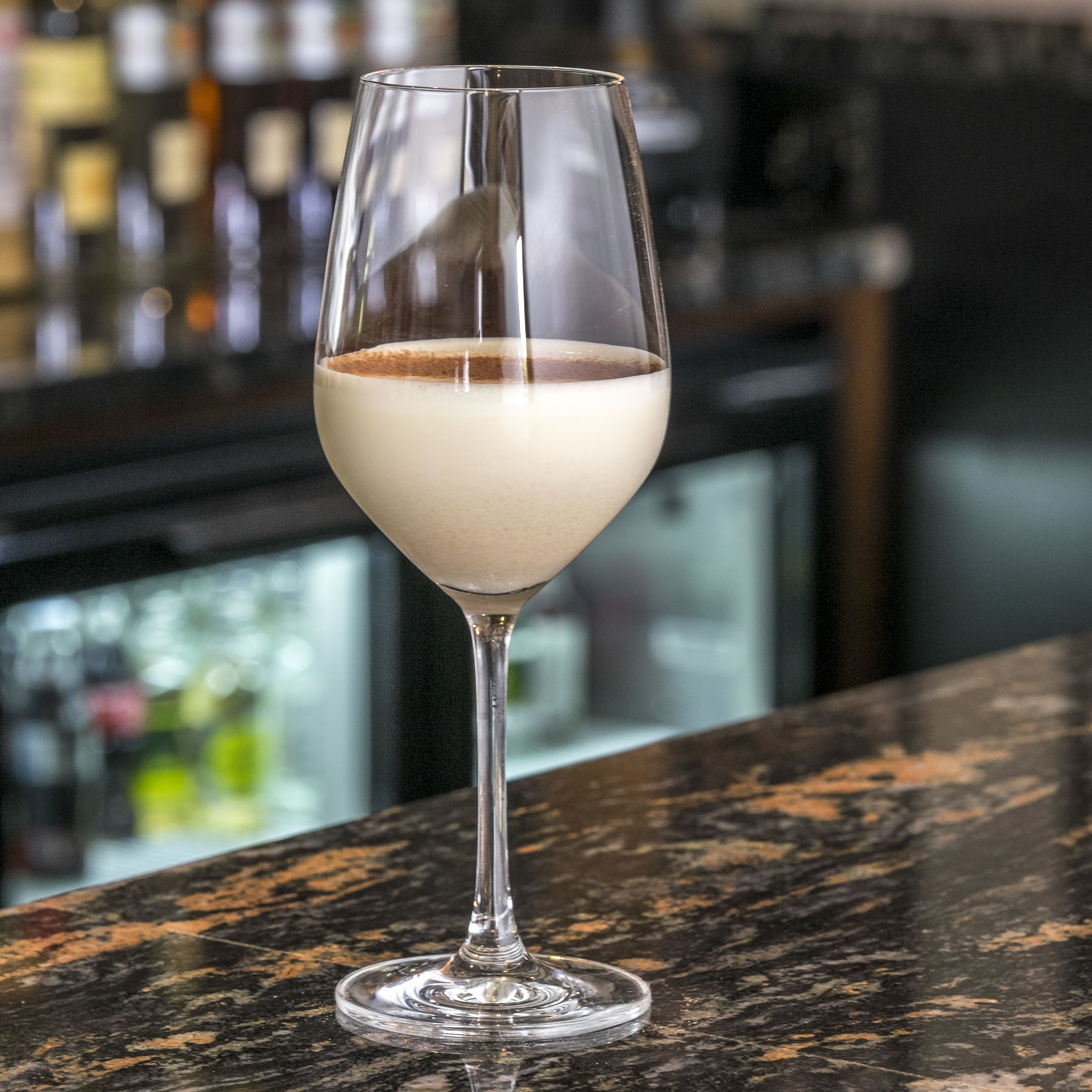 Ett martiniglas med en drink i flera lager, placerat på en bardisk.