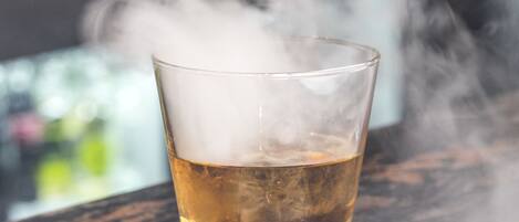 Un verre contenant un liquide ambré, surmonté d’une vapeur fumée, posé sur une surface sombre et texturée.