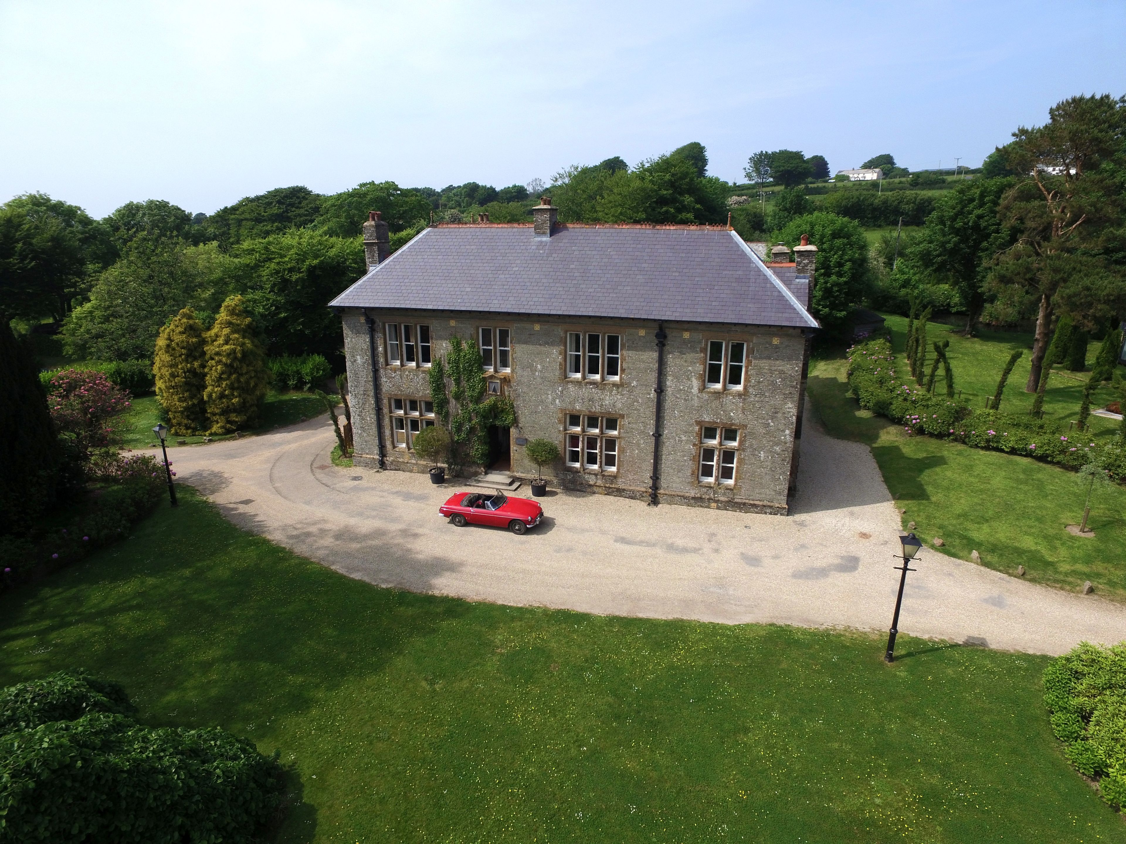 A stone house with a gravel driveway and a red car parked in front.