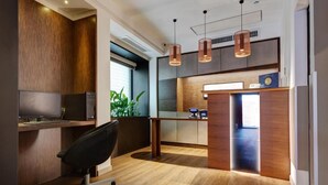 A modern office space with a desk, chair, and computer. There is a reception area with a counter and a plant. - Rome Art Hotel - Trevi Hotels Group (Rome)