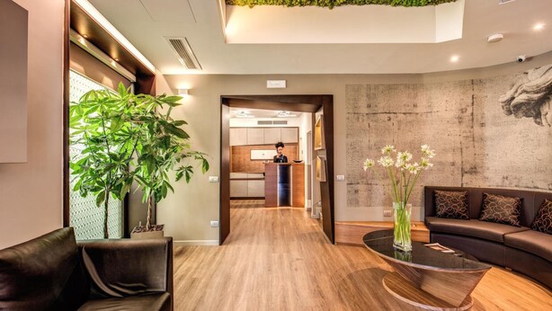 A modern hotel lobby with a wooden floor, a reception desk, a sofa, a coffee table, and a green wall. - Rome Art Hotel - Trevi Hotels Group (Rome)
