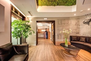 A modern hotel lobby with a wooden floor, a reception desk, a sofa, a coffee table, and a green wall. - Rome Art Hotel - Trevi Hotels Group (Rome)