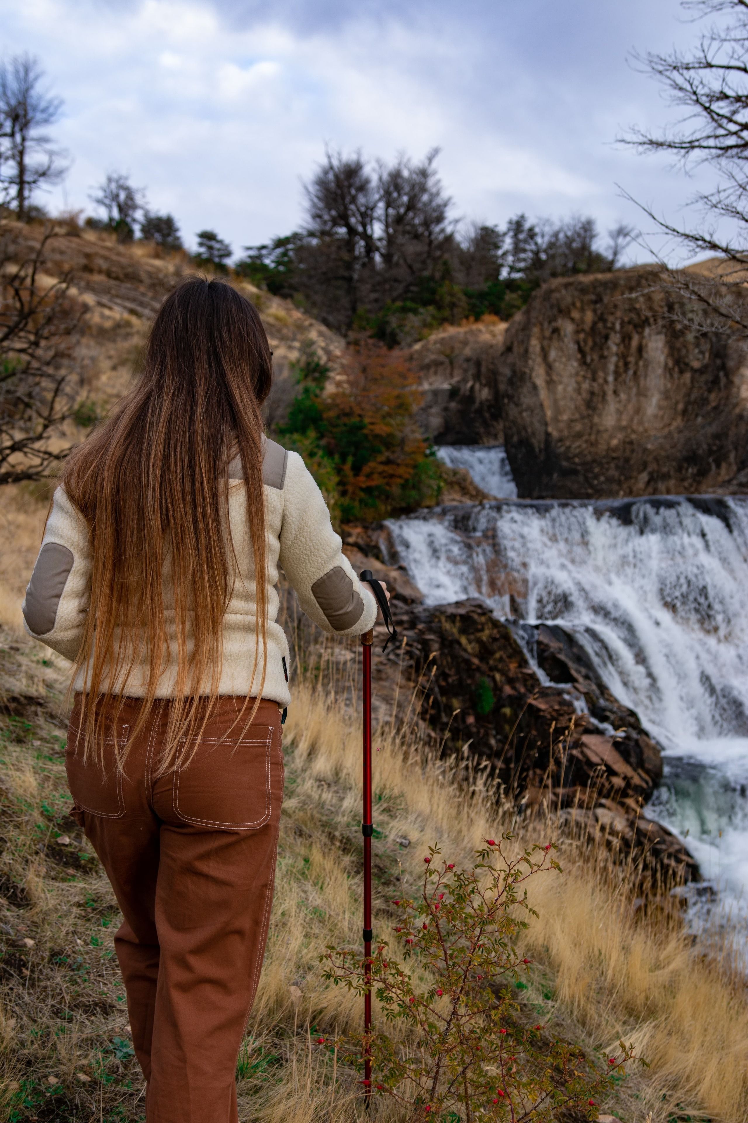 A person standing with a walking stick near a waterfall.