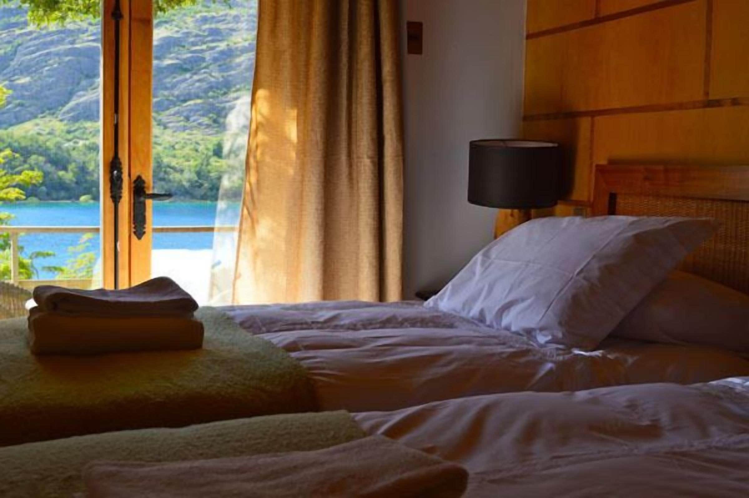 A hotel room with a bed, a window with curtains, and a view of a lake.