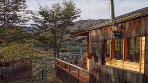 A rustic wooden cabin with a balcony overlooking a lake and forested hills. - Parador Austral Lodge (Chile Chico)