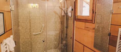 Un baño de cabaña de madera con ducha de vidrio, inodoro, lavabo y espejo.