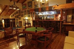 Un área de bar con mobiliario de madera, una mesa de billar y un refrigerador.