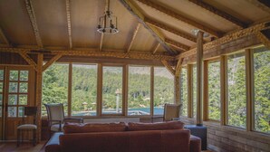 A cozy cabin interior with a large window offering a scenic view of a forested area. - Parador Austral Lodge (Chile Chico)