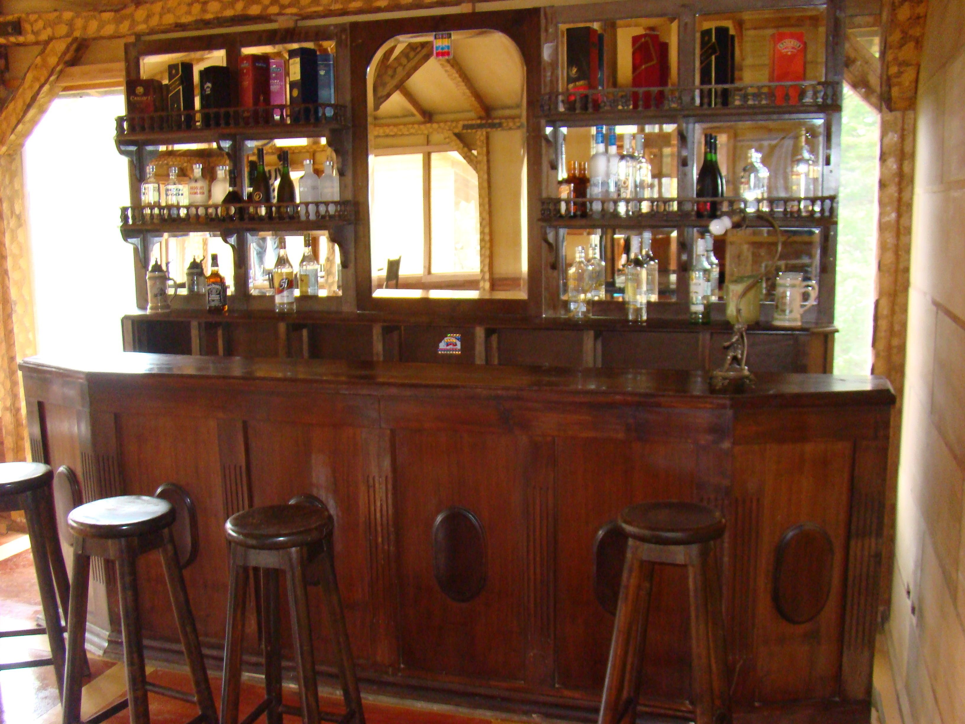 A bar area with wooden bar stools and shelves stocked with bottles.