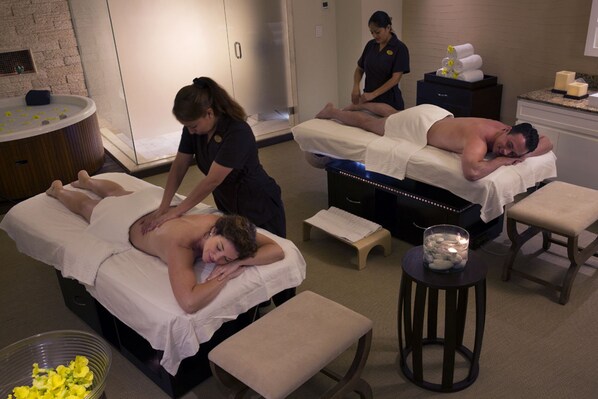 A massage therapy room with two clients receiving treatments, a massage table, and a small table with candles.