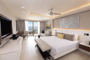 A modern hotel room with a large bed, a flat-screen TV, a desk, and a balcony with a view of the sea. - Royalton Hideaway Riviera Cancun, An Autograph Collection All-Inclusive Resort- Adults Only - Newly Renovated (Puerto Morelos)