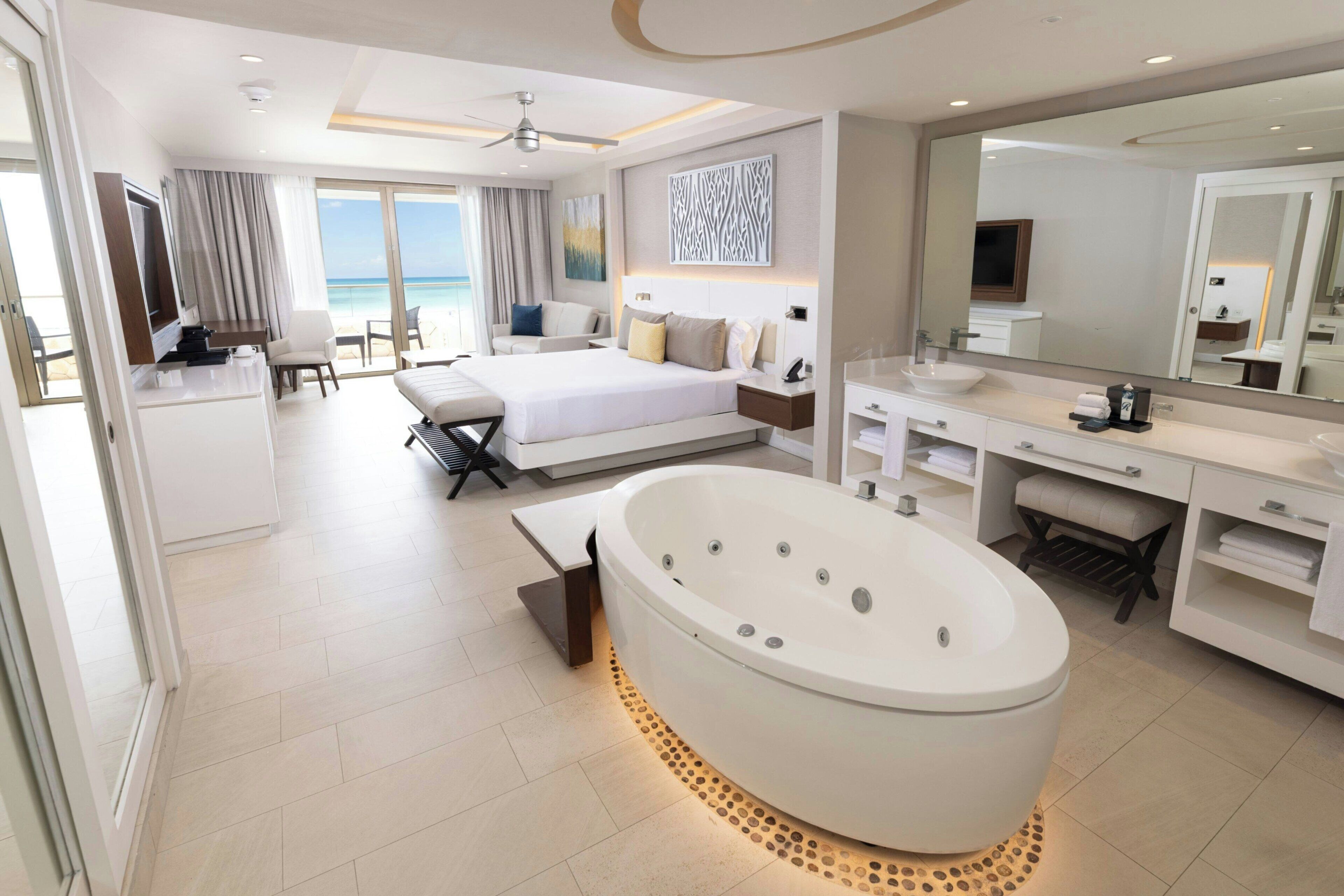 Ein modernes Hotelzimmer mit einem großen Bett, einem separaten Schreibtischbereich, einer Badewanne und einem Badezimmer mit einem großen Spiegel.