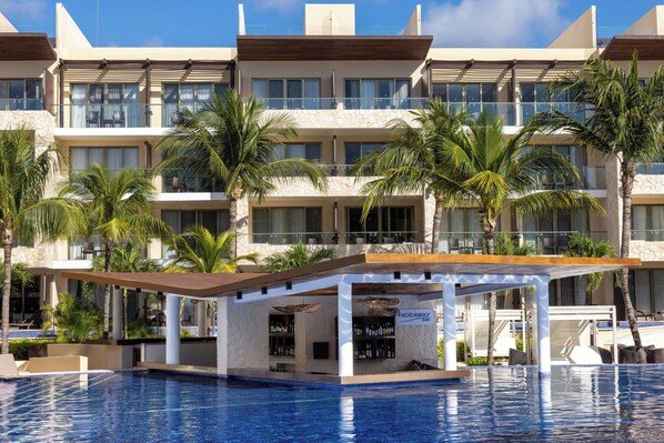A hotel with a pool, palm trees, and a bar area.