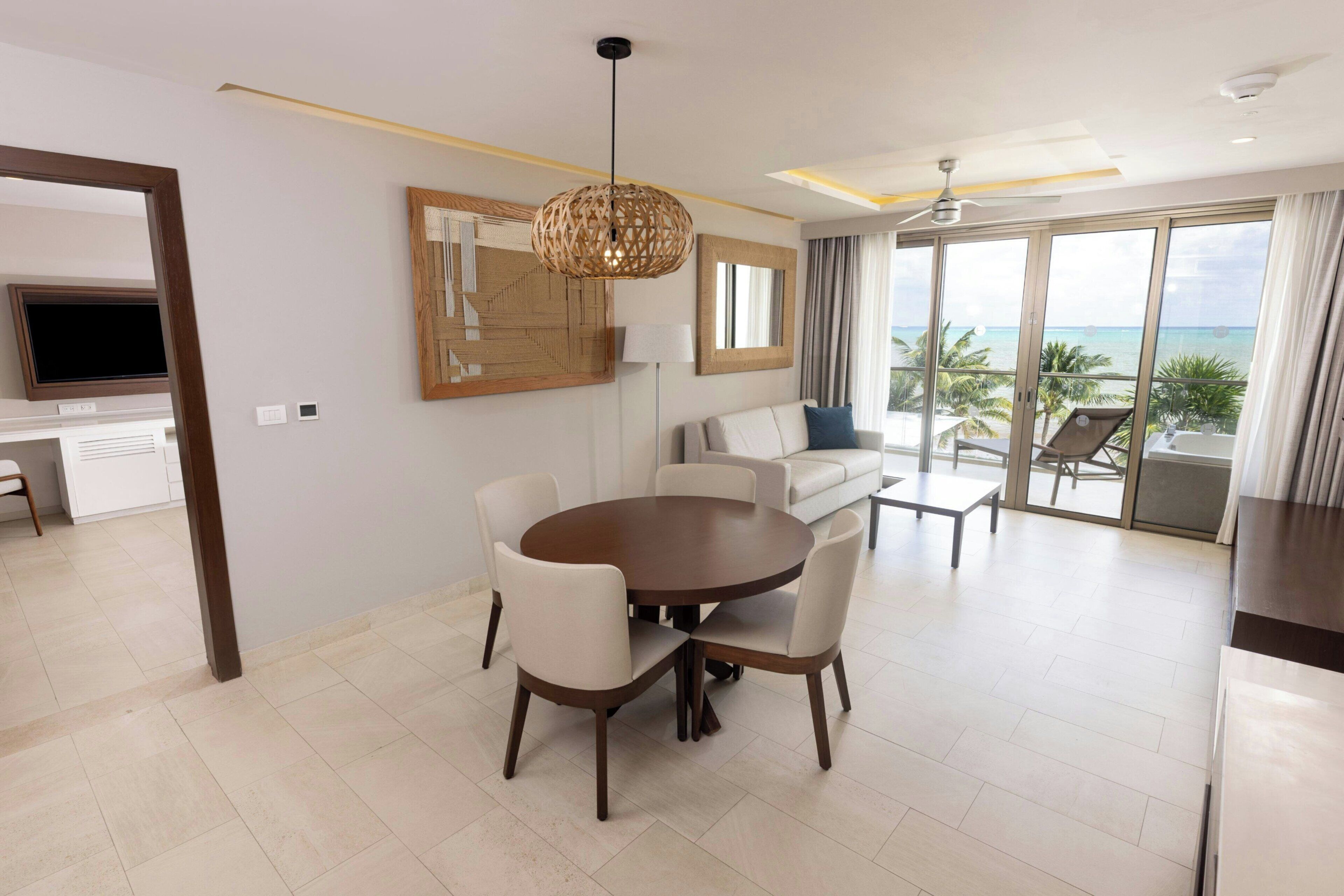 Une chambre d’hôtel moderne dotée d’un coin repas, d’une grande fenêtre offrant une vue dégagée, d’un ventilateur de plafond et d’un téléviseur à écran plat.