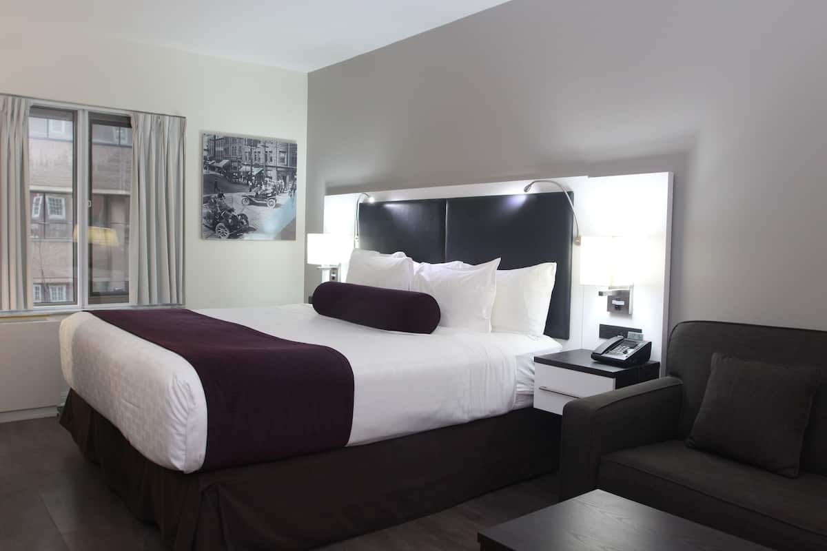 A modern hotel room with a large bed, a bedside table with a phone, a nightstand, a sofa, and a window with curtains.