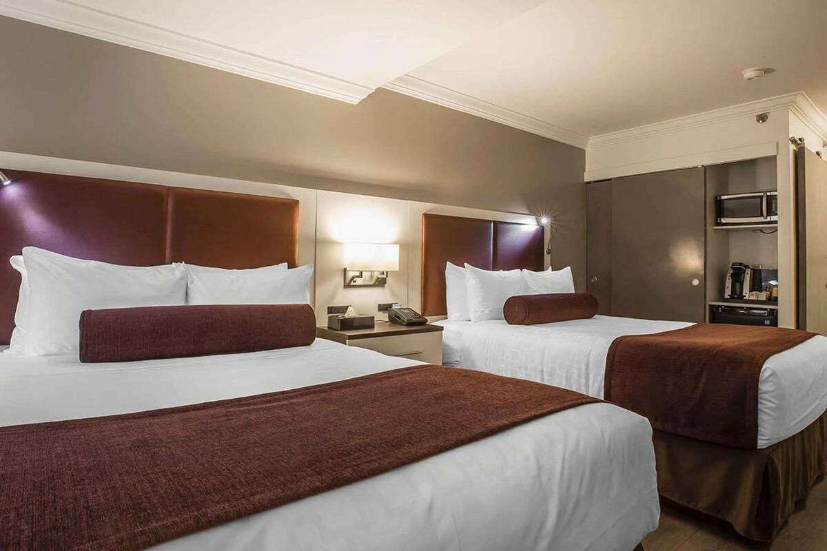 A hotel room with two beds, a nightstand with a lamp, a microwave, and a coffee maker.