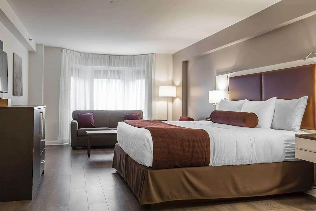 A hotel room with a large bed, a sofa, a desk, and a wardrobe.