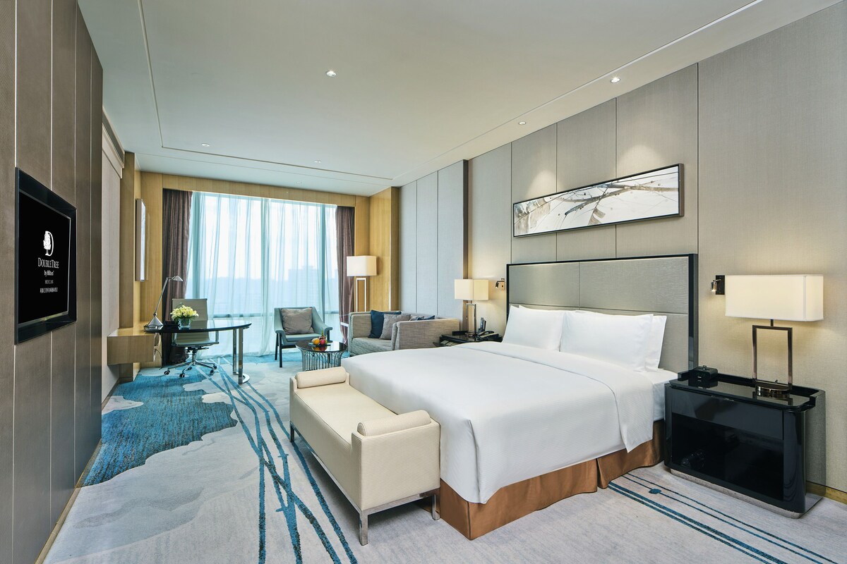 A modern hotel room with a large bed, a desk, a sofa, and a TV.