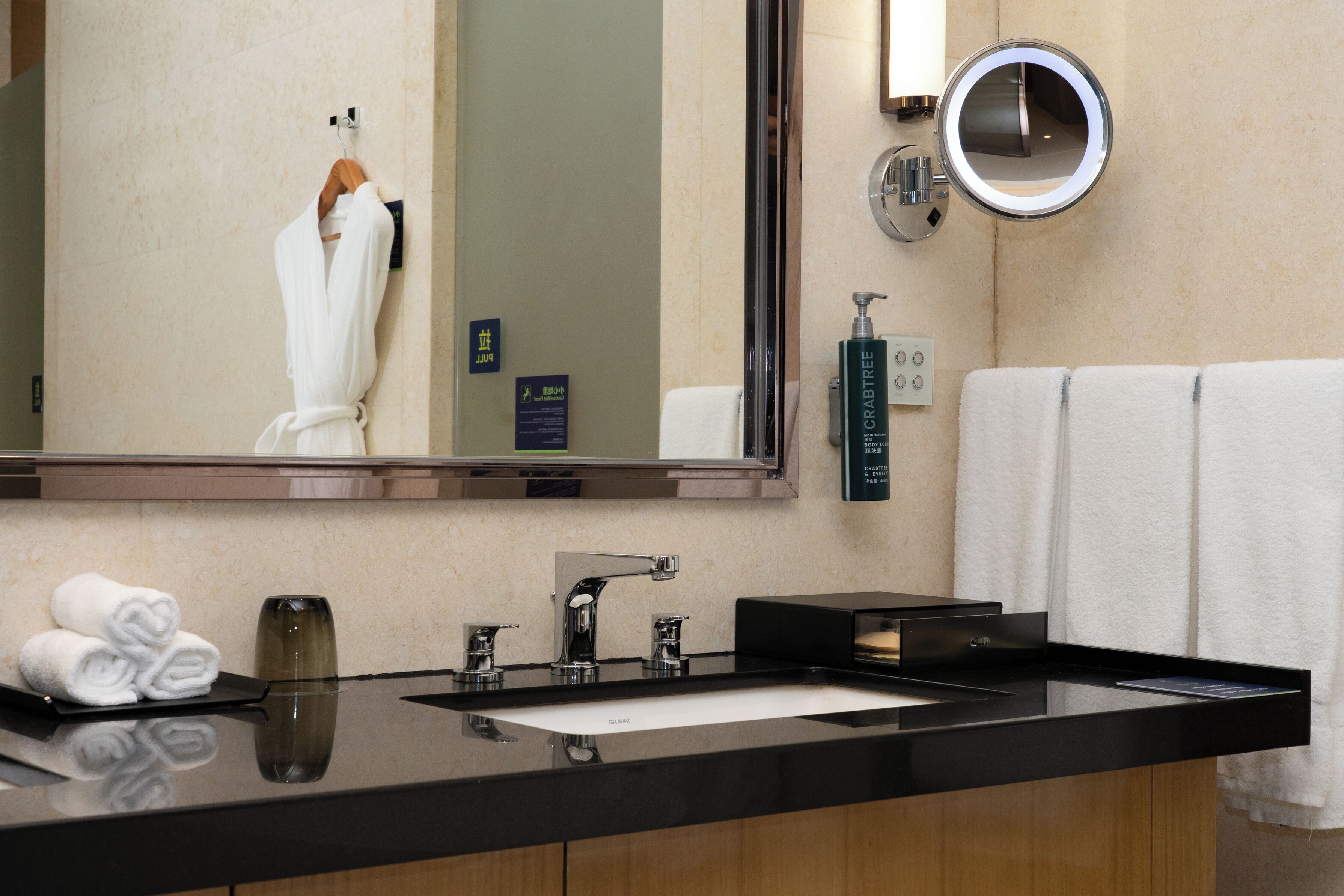 A bathroom with a large mirror, a sink, a towel rack, and a bottle of body lotion.