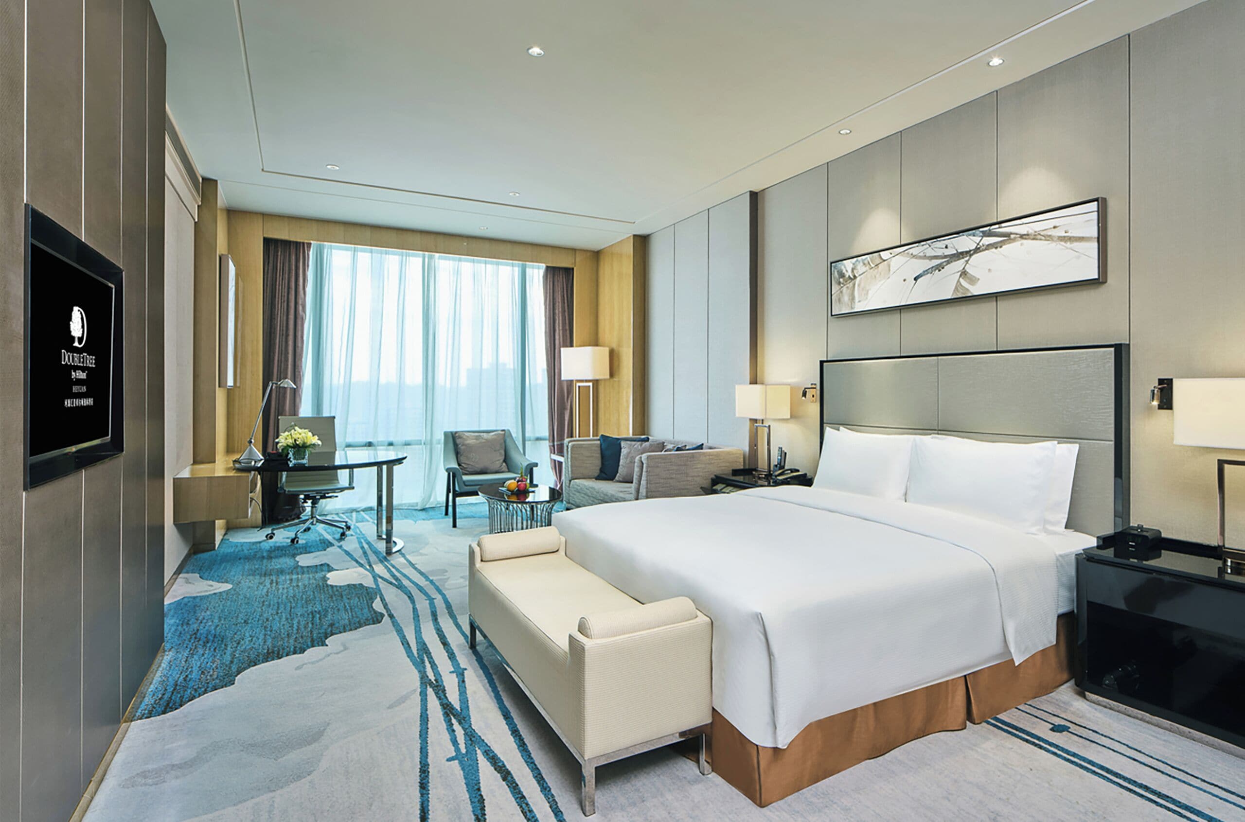A hotel room with a large bed, a desk, a chair, a sofa, and a TV.