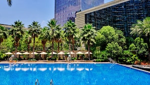 A swimming pool with lounge chairs and umbrellas, surrounded by palm trees and modern buildings. - DoubleTree by Hilton Hotel Heyuan (Heyuan)