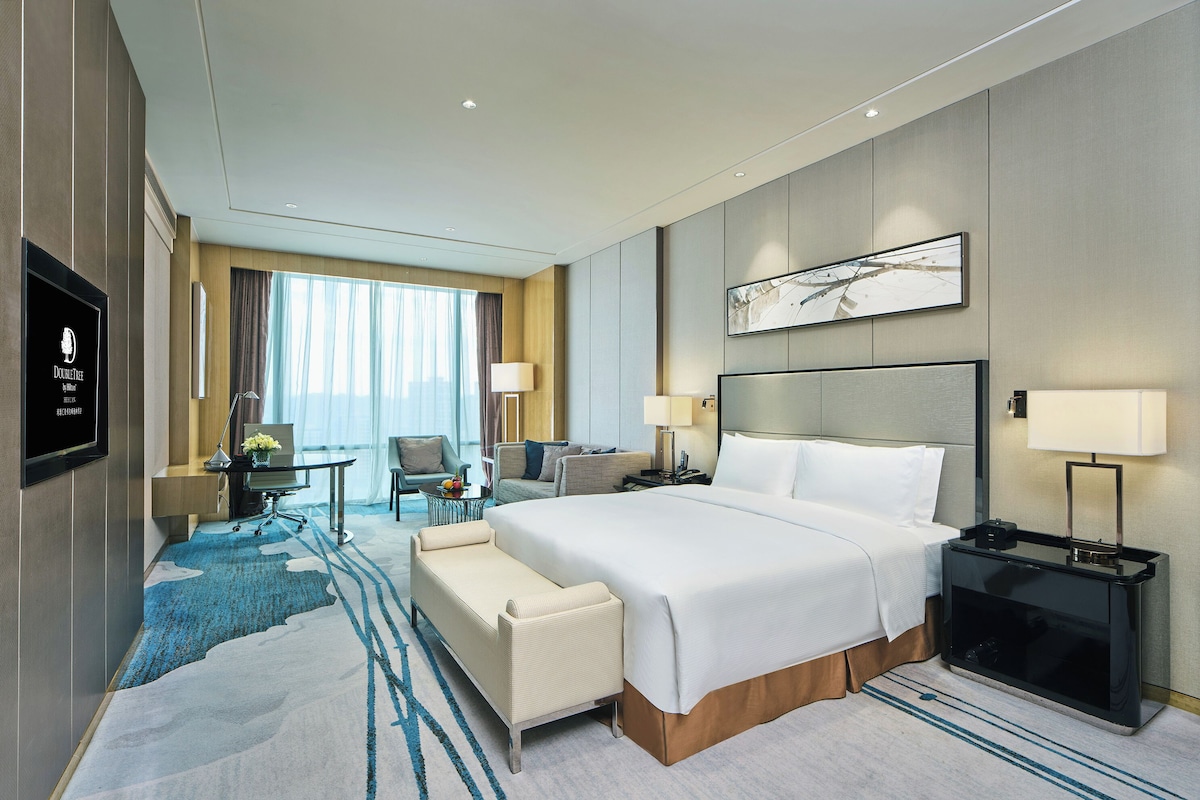 A modern hotel room with a large bed, a desk, a sofa, and a TV.
