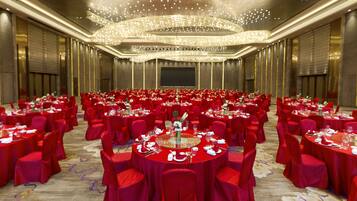 Un amplio salón de banquetes con mesas redondas cubiertas con manteles rojos y sillas rojas, dispuestas en filas.