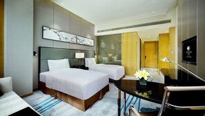 A hotel room with two beds, a desk, a chair, a TV, and artwork on the wall.
