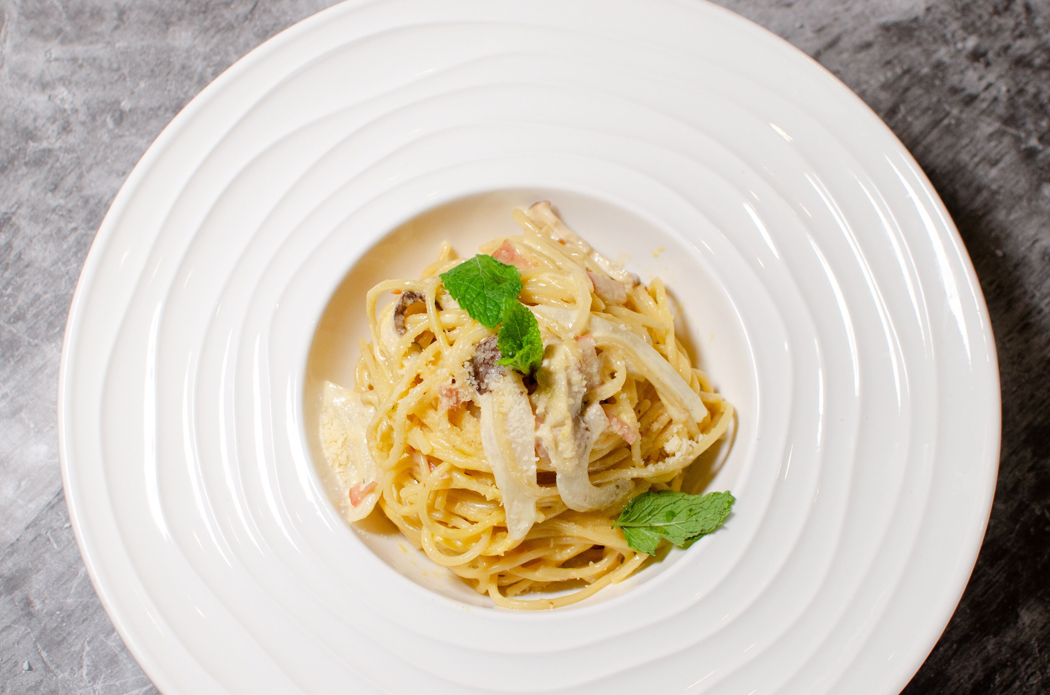 Une assiette de spaghettis nappées d’une sauce crémeuse, garnie d’une feuille de menthe.