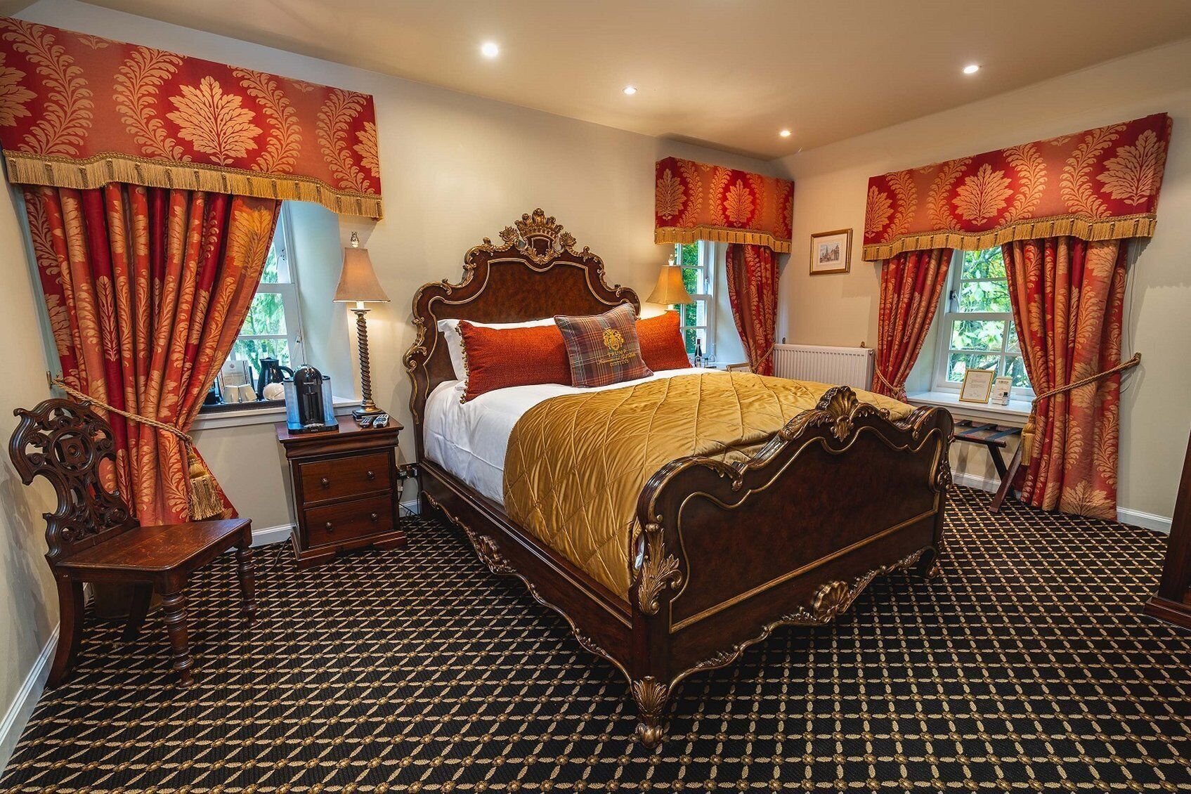 A traditional bedroom with a large bed, ornate curtains, and a patterned carpet.