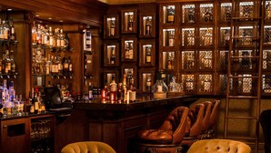 A bar area with wooden cabinets, leather chairs, and a chandelier. - Trump® International Scotland (Aberdeen)