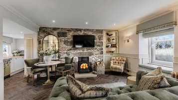 A living room with a stone fireplace, a television mounted above it, and a cozy seating area with a sofa and armchairs.