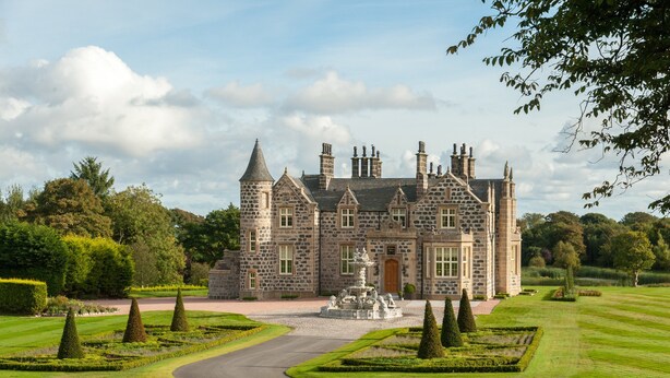 A large stone building with multiple chimneys and a central entrance. - Trump® International Scotland (Aberdeen)