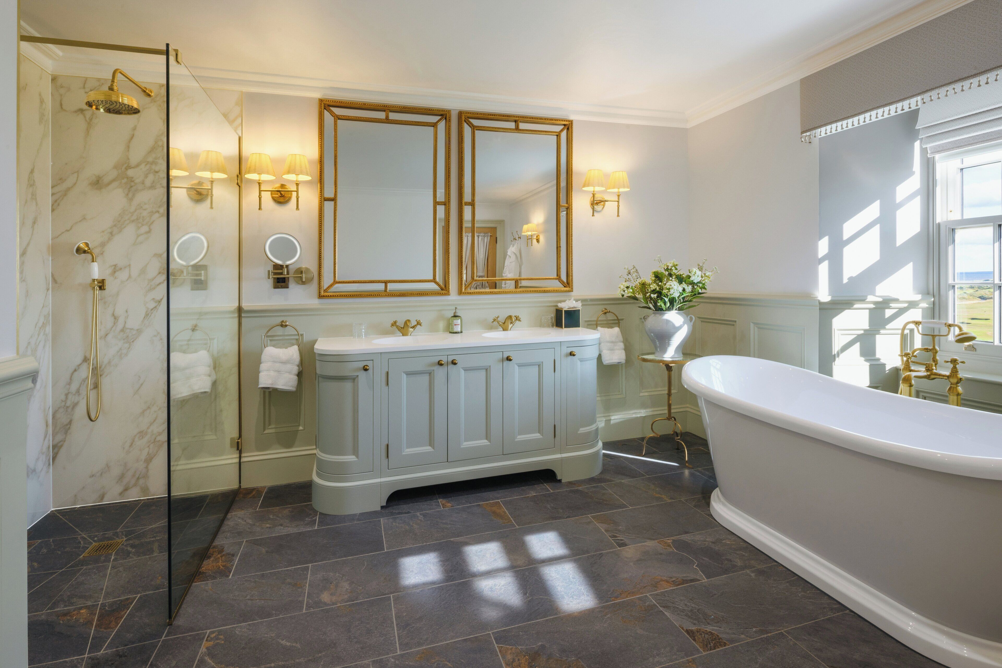 A bathroom with a marble shower, a freestanding bathtub, and a vanity with a double mirror.