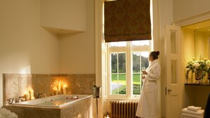 A bathroom with a bathtub, candles, and a view of a garden. - Trump® International Scotland (Aberdeen)