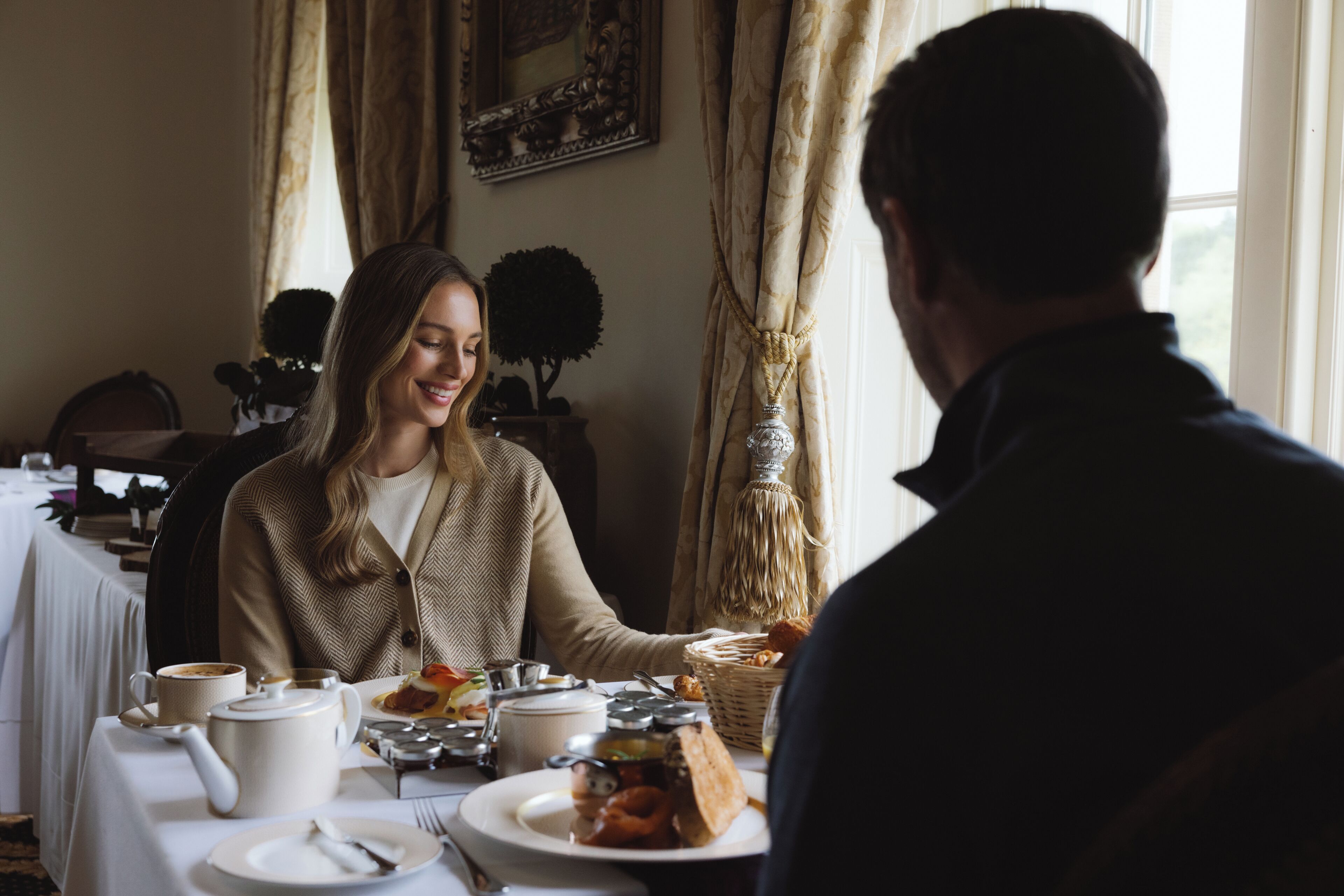 A dining table with plates of food, a teapot, and a candle.