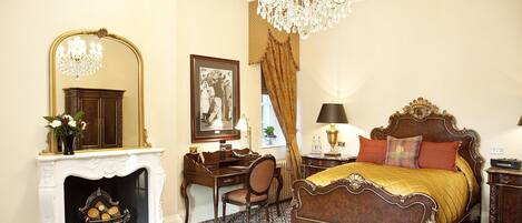 A classic bedroom with a four-poster bed, a desk, a fireplace, and a chandelier.